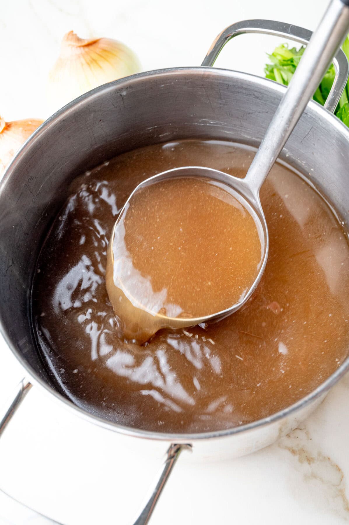 Strained beef stock in a pot and being poured from a ladle.