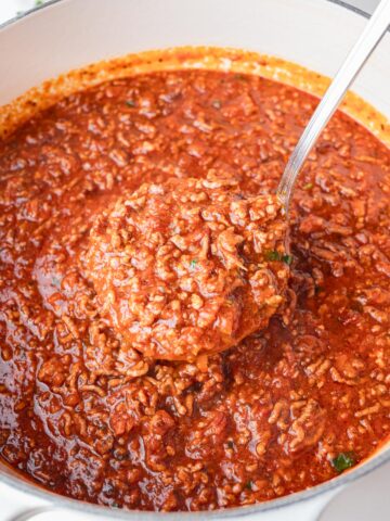 Spaghetti meat sauce in a white pot with a ladle inside.