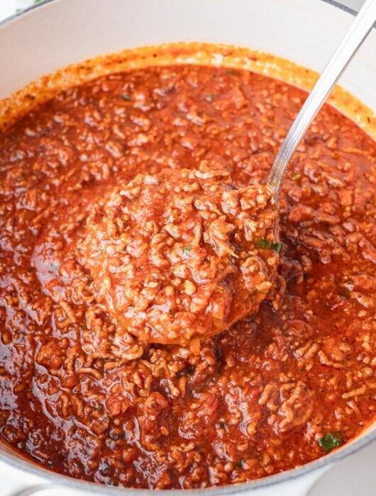 Spaghetti meat sauce in a white pot with a ladle inside.