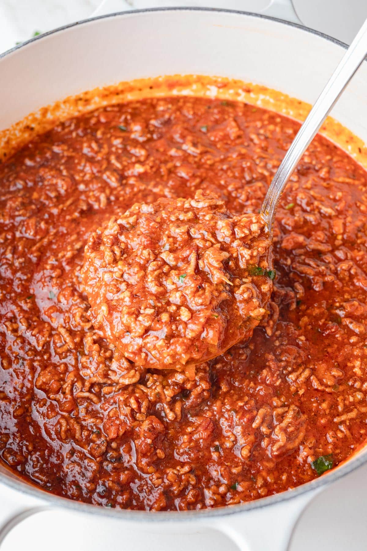 Spaghetti meat sauce in a white dutch oven with a ladle inside.