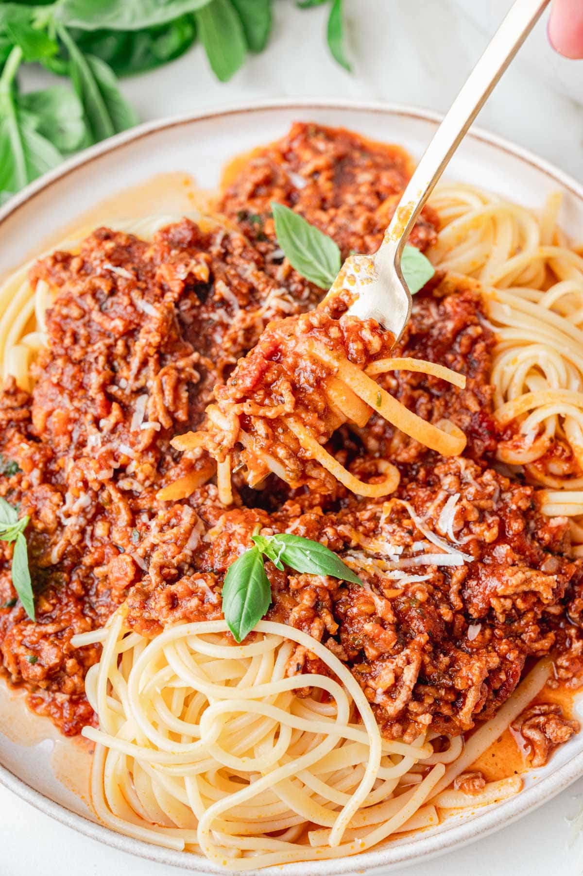 Spaghetti pasta with meat sauce on top on a beige plate. Some of the spaghetti is on a fork.