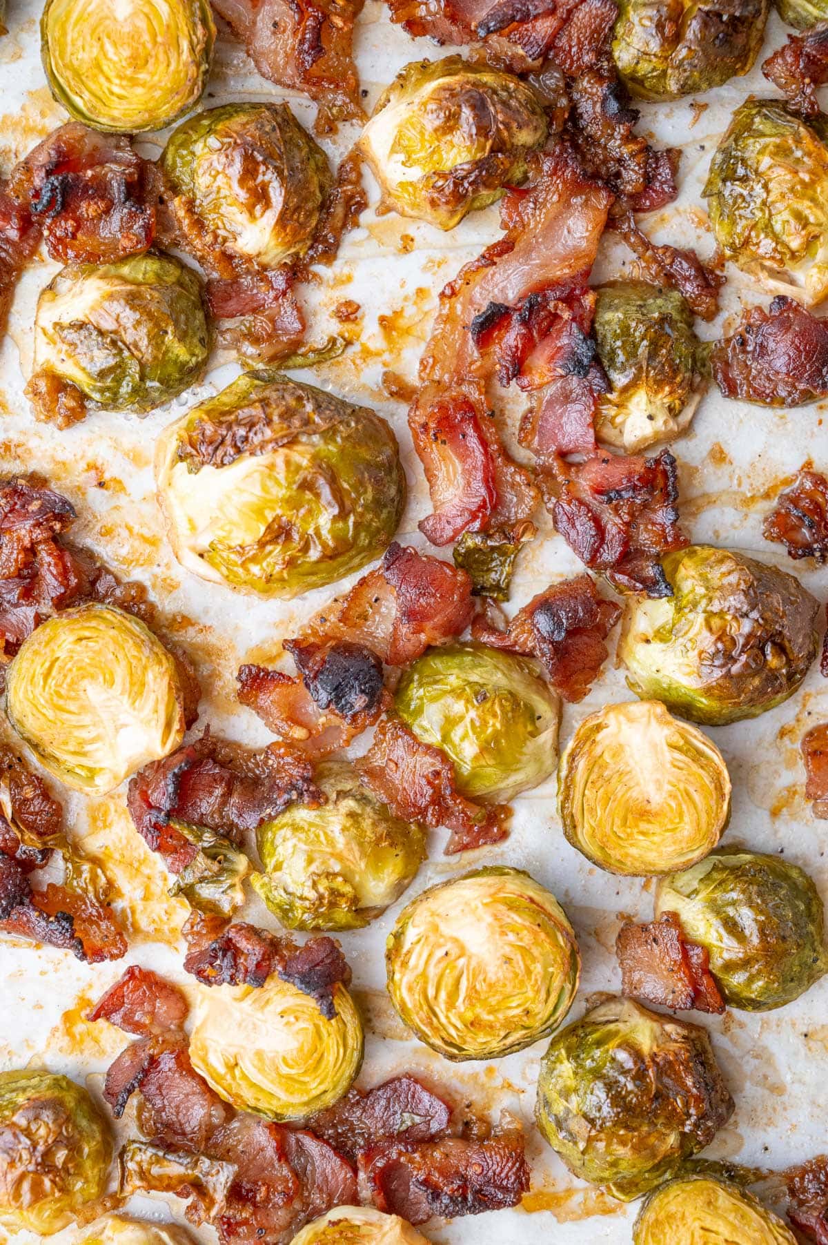 A close-up photo of roasted Brussels sprouts with bacon on a baking sheet.