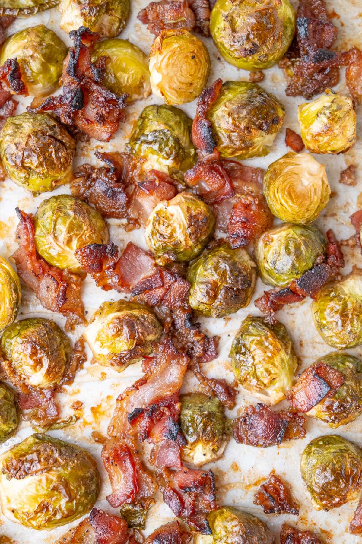 A close-up photo of roasted Brussels sprouts with bacon on a baking sheet.