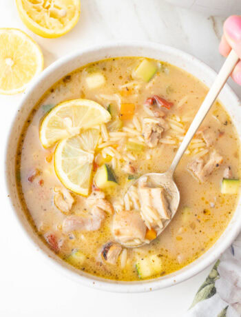 Lemon chicken orzo soup in a beige bowl with two lemon slices on top.