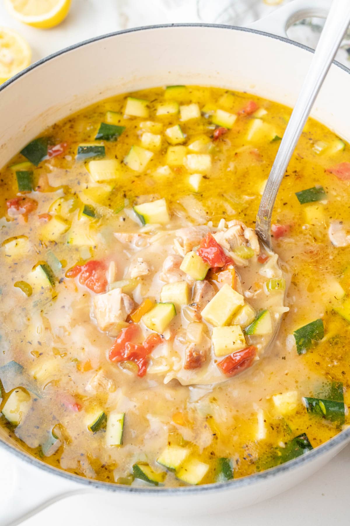 Lemon chicken orzo soup in a large Dutch oven, with a portion being scooped out using a ladle.