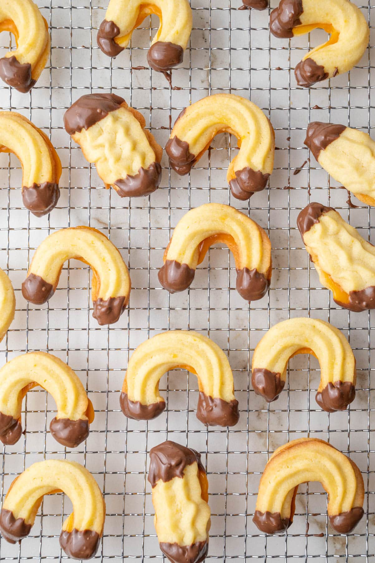 Linzer Kipferl with apricot jam and dipped in chocolate on a cooling rack.