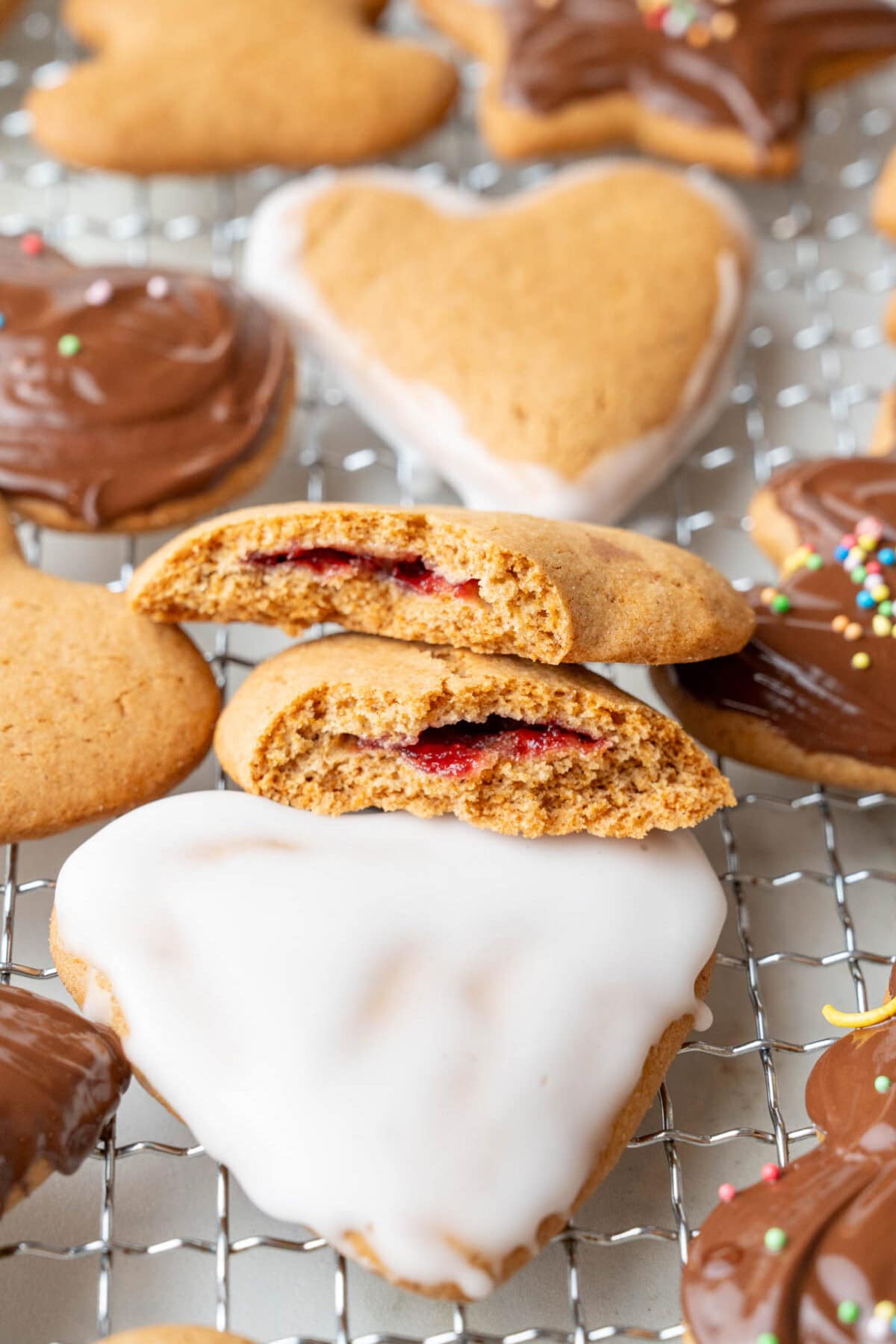 A close up photo of pierniczki cookies stuffed with plum preserves. More cookies on a cooling rack.