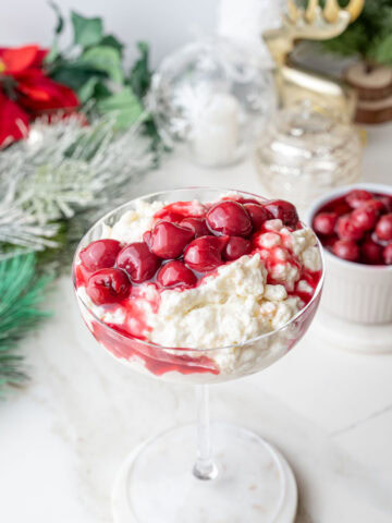 Risalamande with cherry sauce in a cocktail glass. Christmas decorations in the background.