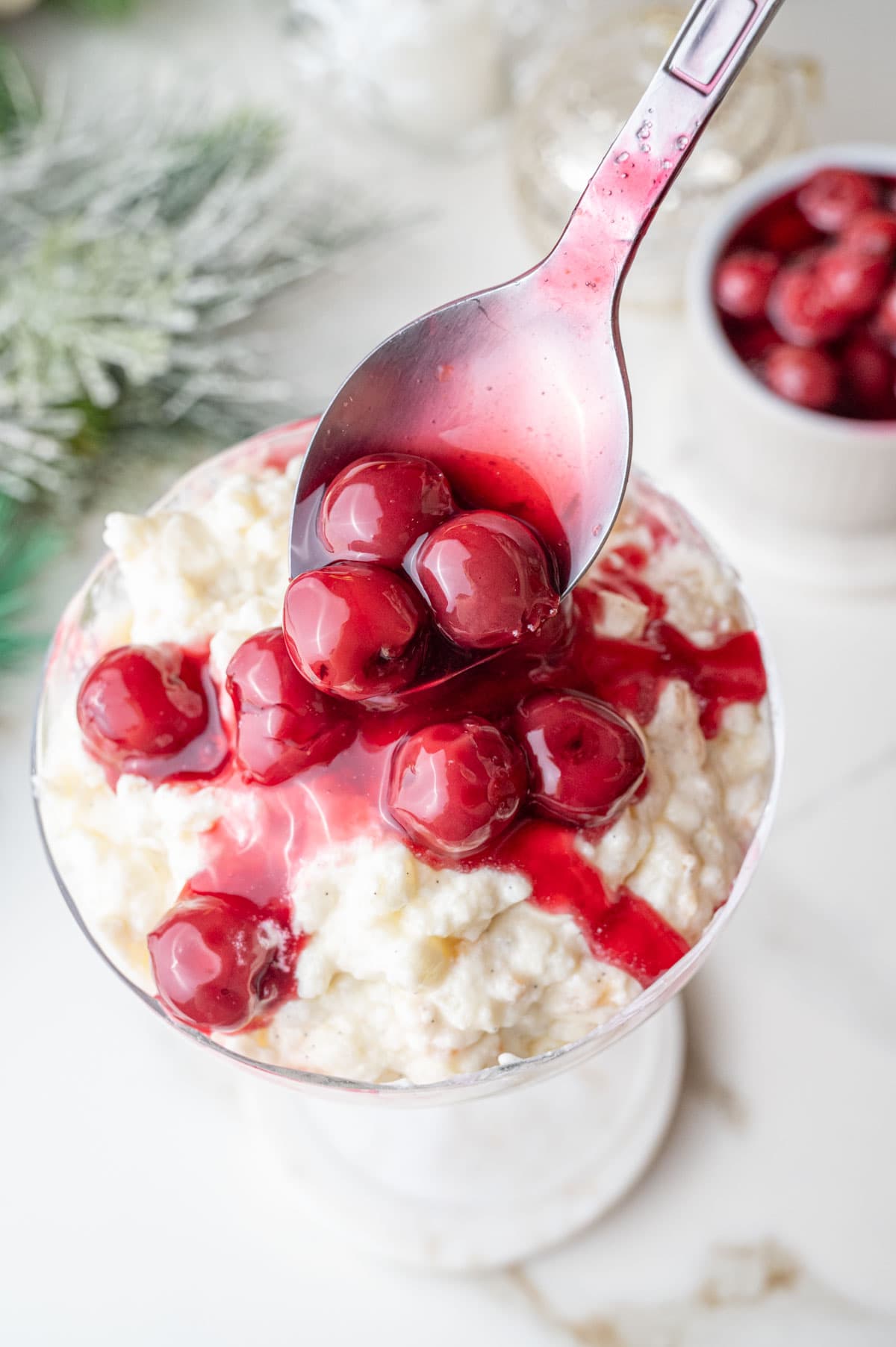 Cherry sauce is being spooned over a Risalamande in a cocktail glass.