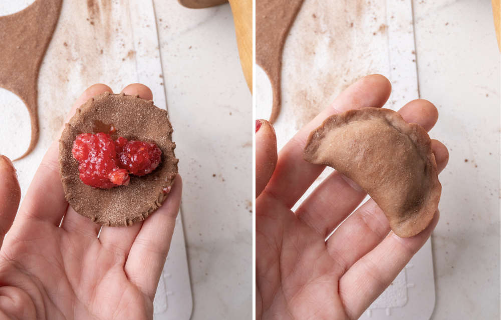 The left image shows a hand holding a circular piece of chocolate dough with fresh raspberries as the filling. The right image displays the same dough folded over and sealed into a half-moon shape, forming a pierogi ready for cooking.